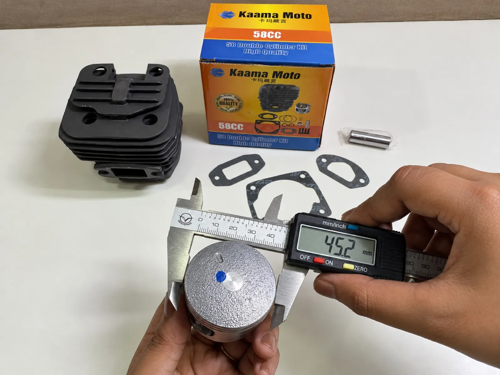 A piston being measured with a digital caliper beside a Kaama Moto 58CC cylinder kit